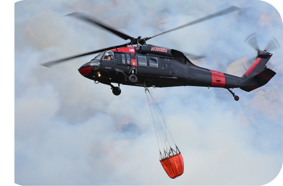 A helicopter is flying through the air with a red object hanging from it. Description generated by AI
