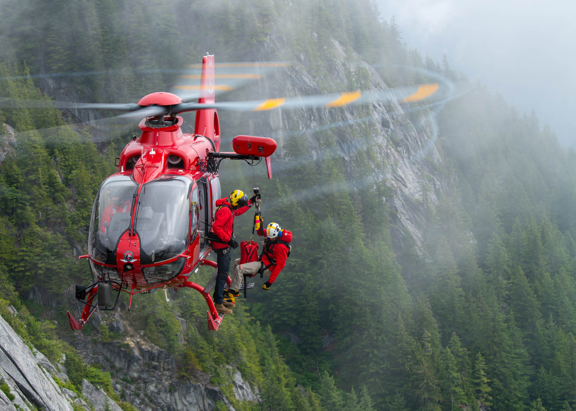 A red and white helicopter flying over a mountain. Description generated by AI