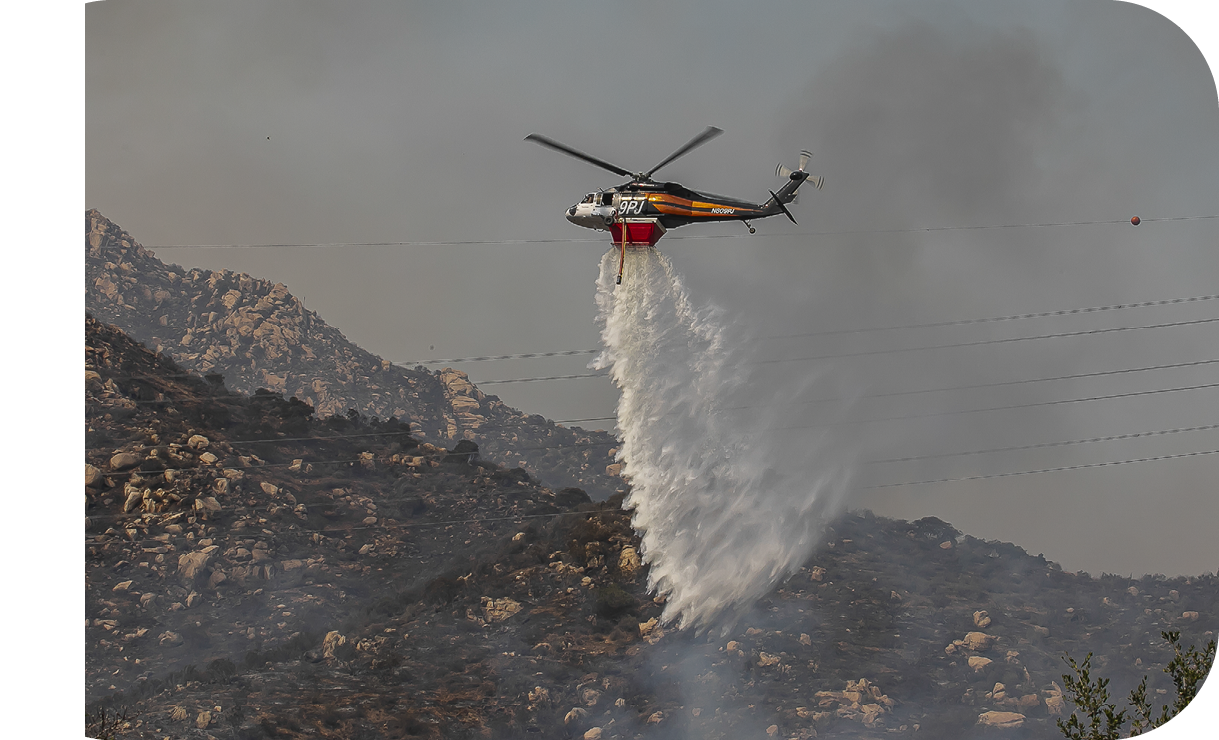 A helicopter is spraying water on a mountain. Description generated by AI