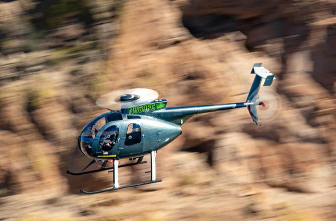 A helicopter flying over a rocky hill. Description generated by AI