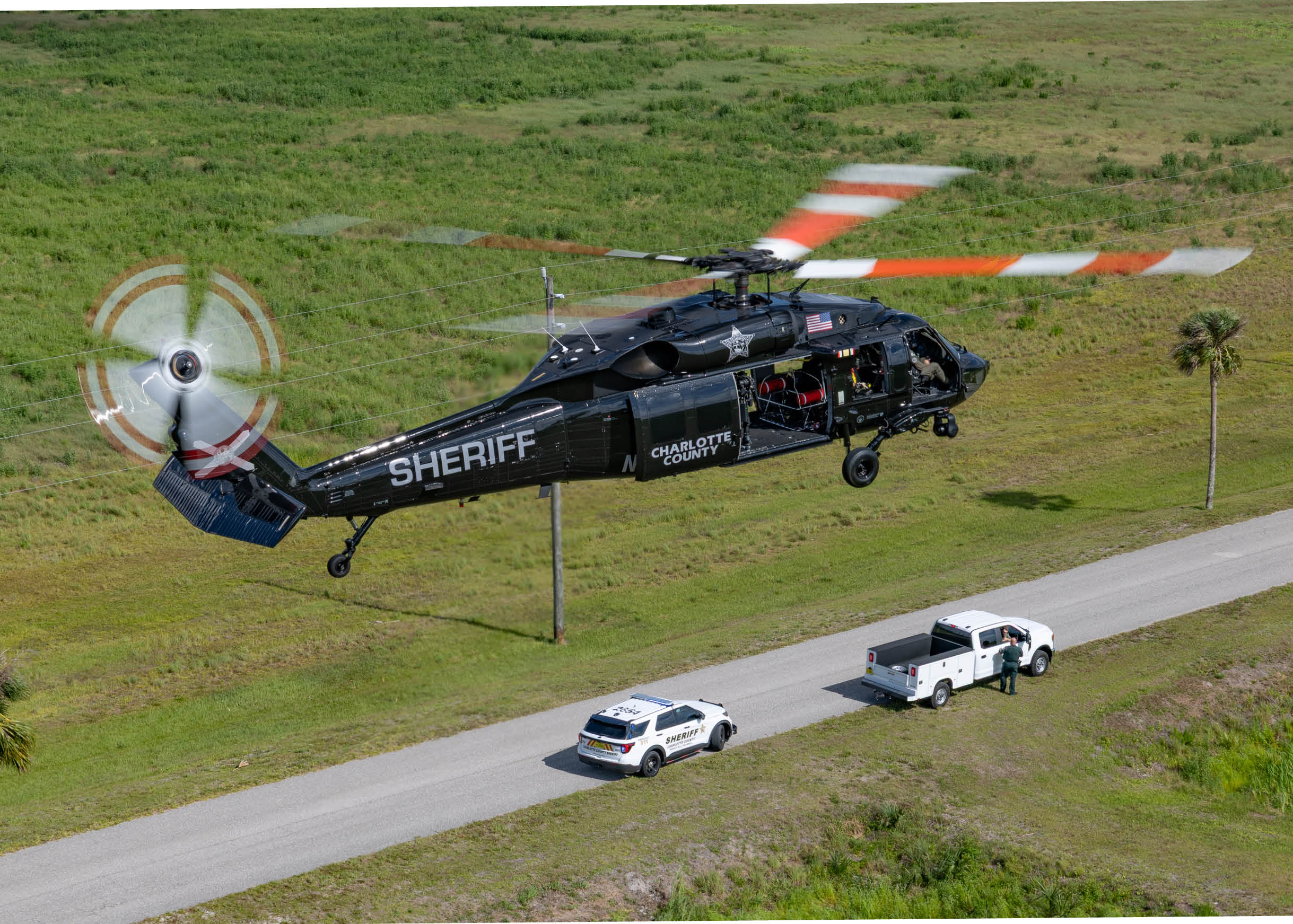 A sheriff helicopter flying over a road with a truck and a car. Description generated by AI