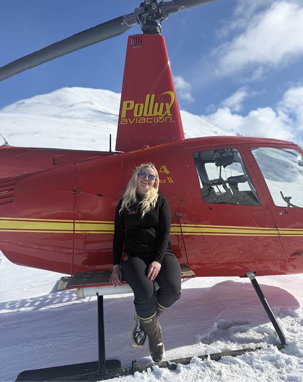 A woman wearing a blue shirt and sunglasses is sitting in a helicopter. Description generated by AI