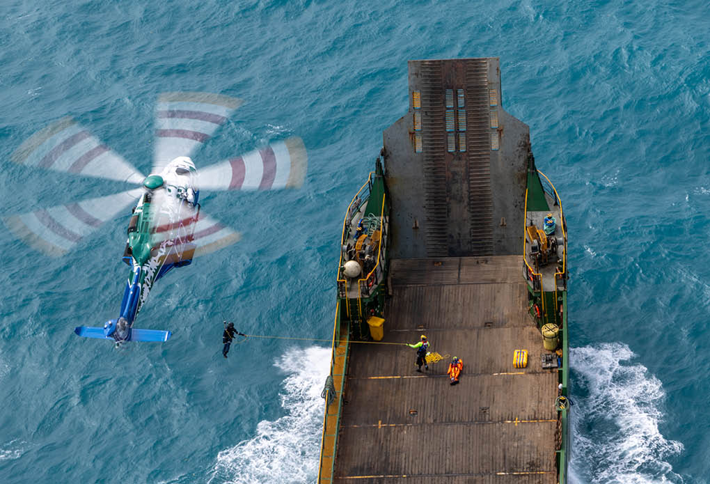 A helicopter flying over the ocean with a shark swimming below. Description generated by AI