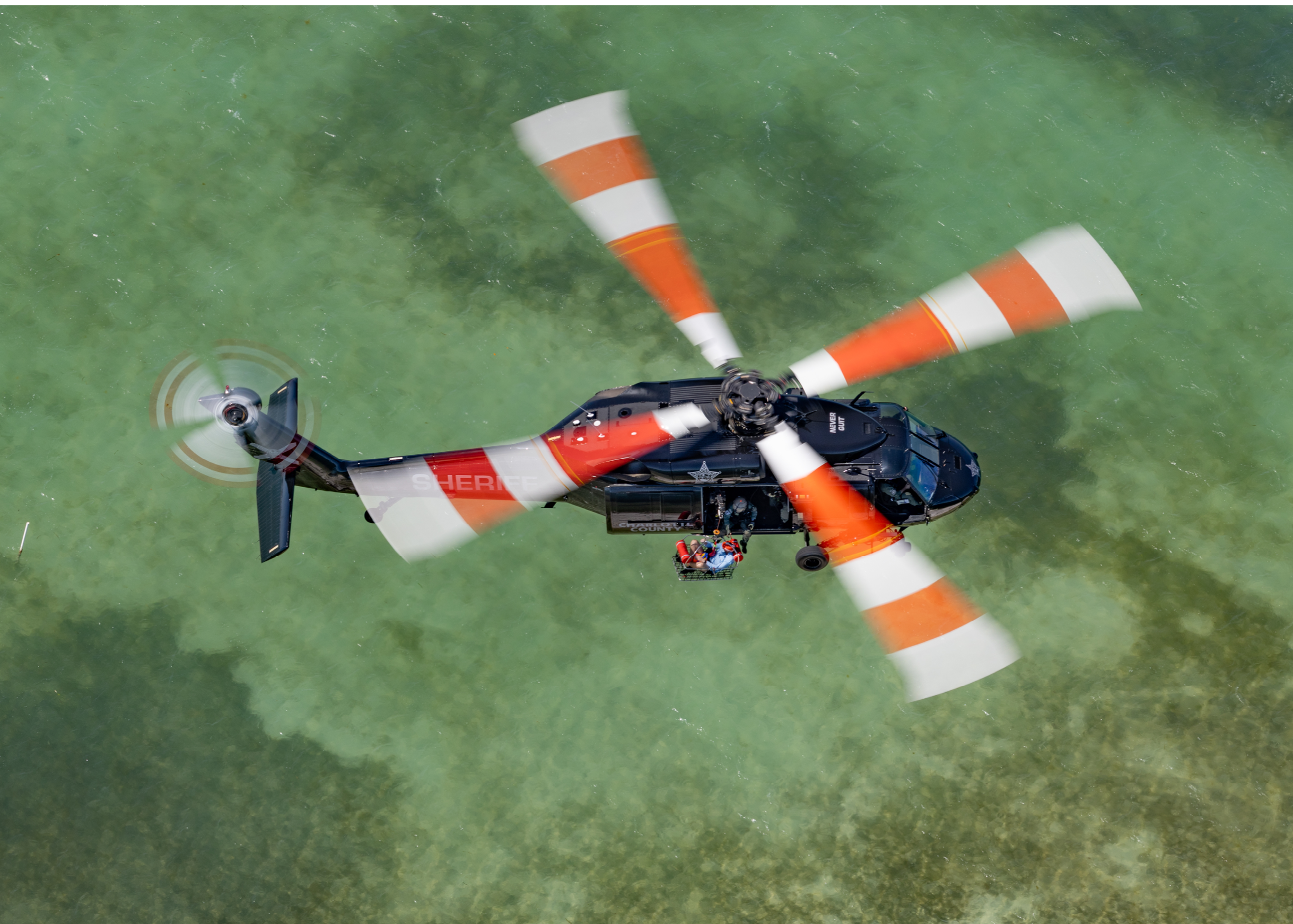 A black helicopter with a red cross on it is flying over a field. Description generated by AI