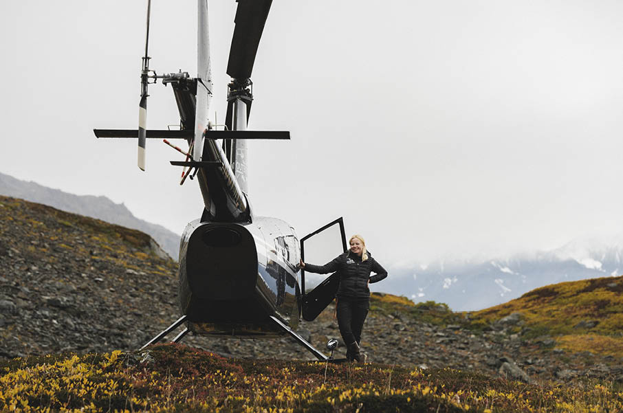 A woman in a blue shirt and jeans standing in front of a helicopter. Description generated by AI