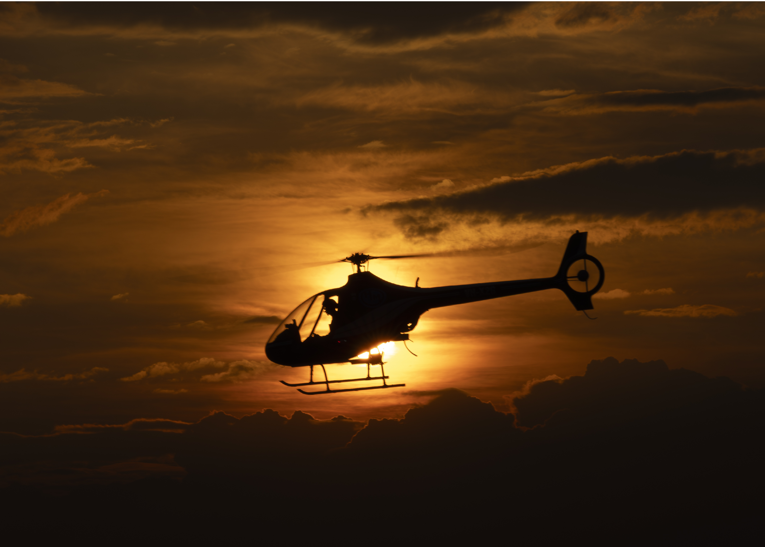 A black helicopter flying over a beach. Description generated by AI