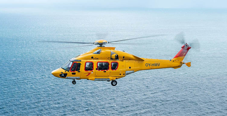 A yellow helicopter with red accents is flying over a calm blue ocean. Description generated by AI