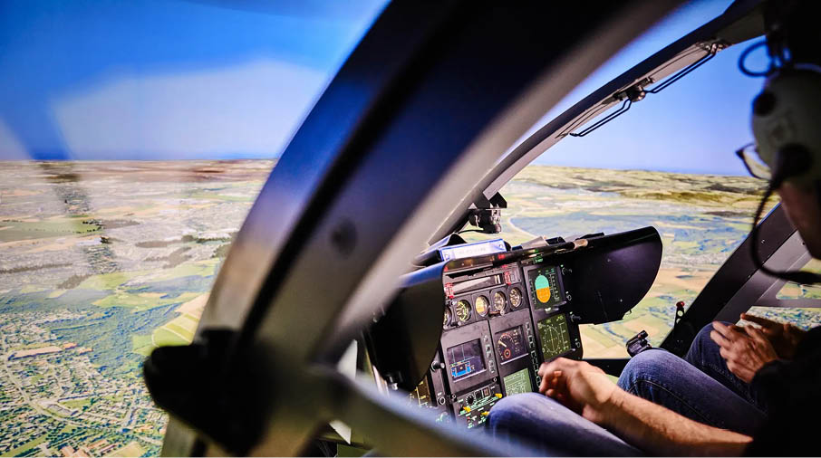 A person in a green jacket is operating controls inside a cockpit with multiple digital display screens. Description generated by AI