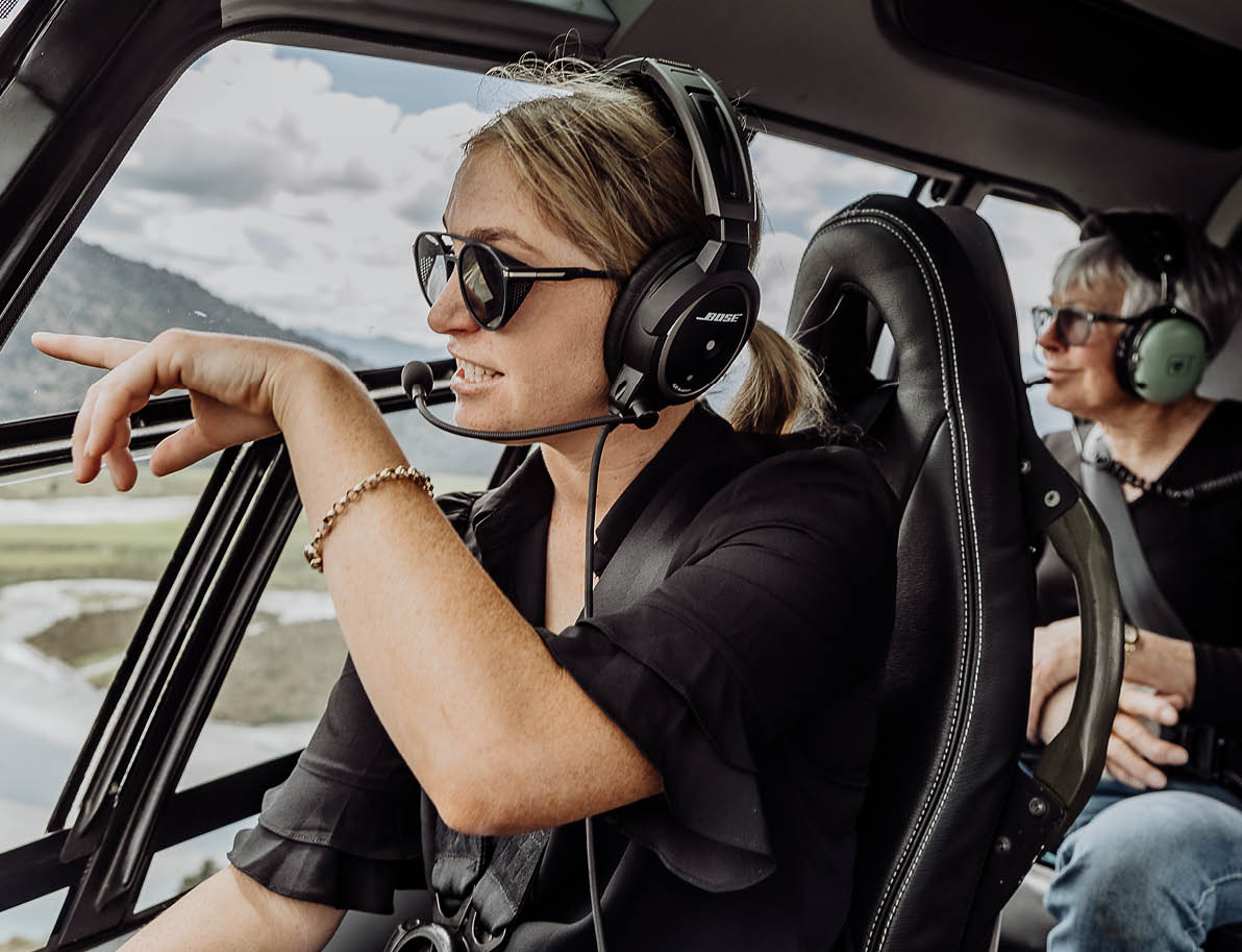 Two adults wearing headsets are seated inside a small aircraft, with one pointing outside the window while the other looks on. Description generated by AI