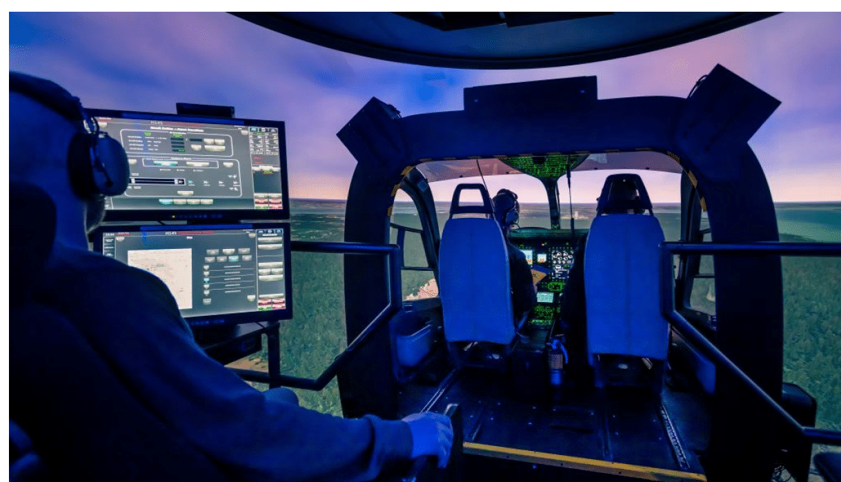 A person wearing headphones is seated inside a flight simulator cockpit with multiple screens displaying flight controls and a view of a virtual landscape outside. Description generated by AI