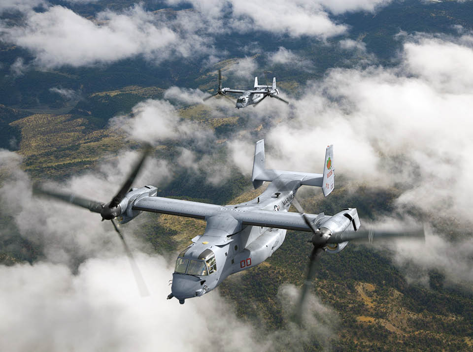 Two military tiltrotor aircraft are flying above a landscape with scattered clouds. Description generated by AI