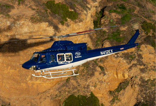 A blue helicopter with the registration N412EX is flying close to a rocky, brown cliffside. Description generated by AI