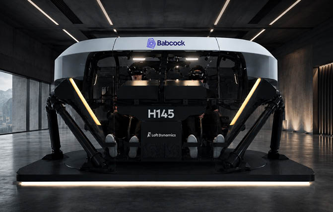 A futuristic robotic device with multiple articulated legs is displayed on a platform in a dimly lit industrial space with the logos Babcock and Loft Dynamics visible on it. Description generated by AI