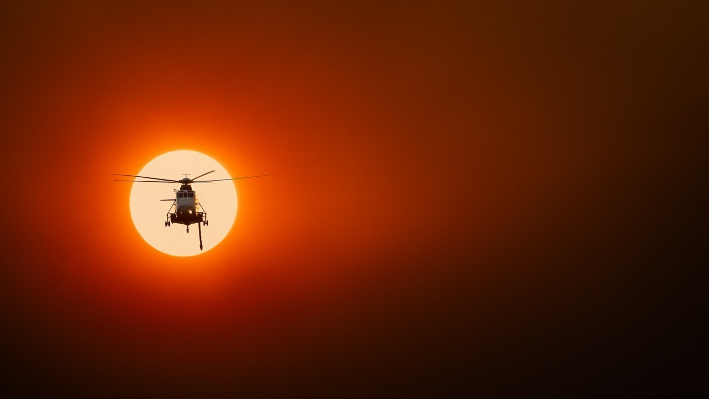 A Sikorsky S61N fire bomber returns to base after a long day on the Grampians Fire Grounds. The sun is smothered in thick bushfire smoke,
creating a thick muddy scene, framing the helicopter in an apocalypse now type energy, not too dissimilar to the daily battle to overcome
the flames and destruction that transpire below on a daily basis