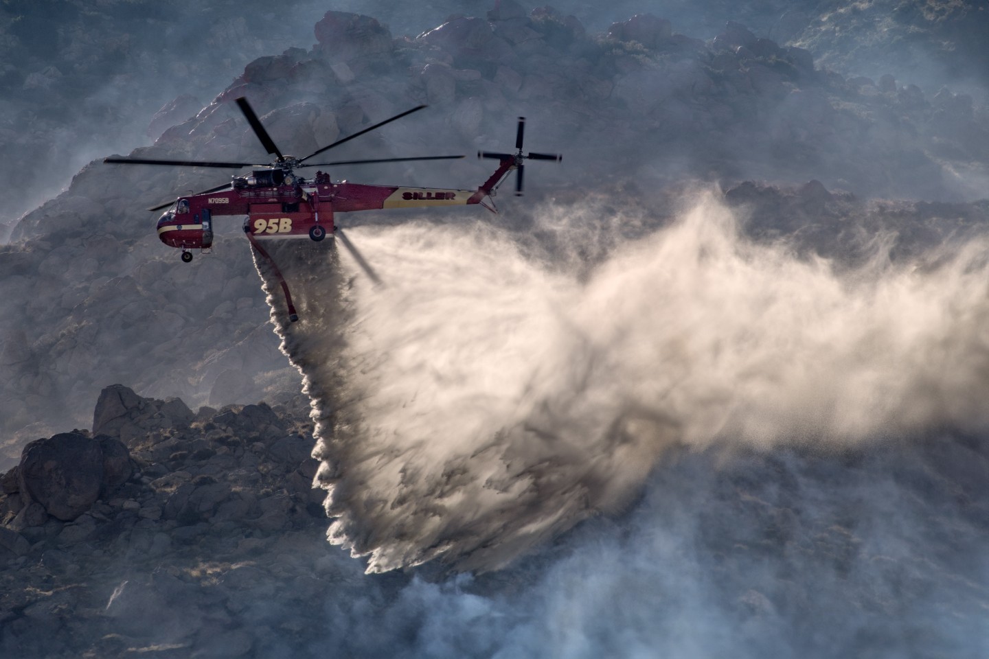 The winds at the Elm Fire near Cabazon, California were extremely strong and it was<br />
really difficult to hold my camera still, especially with my Nikon 200mm to 500mm f/5.6 lens. In<br />
addition, the mountainous terrain made it more challenging to photograph. However, finding the<br />
right position produced some really dynamic photographs, especially this one taken close up to highlight the helicopter's abilities.
Watching Siller’s Skycrane, with their amazing pilots,<br />
maneuver in the adverse weather and mountainous area, was amazing to document.