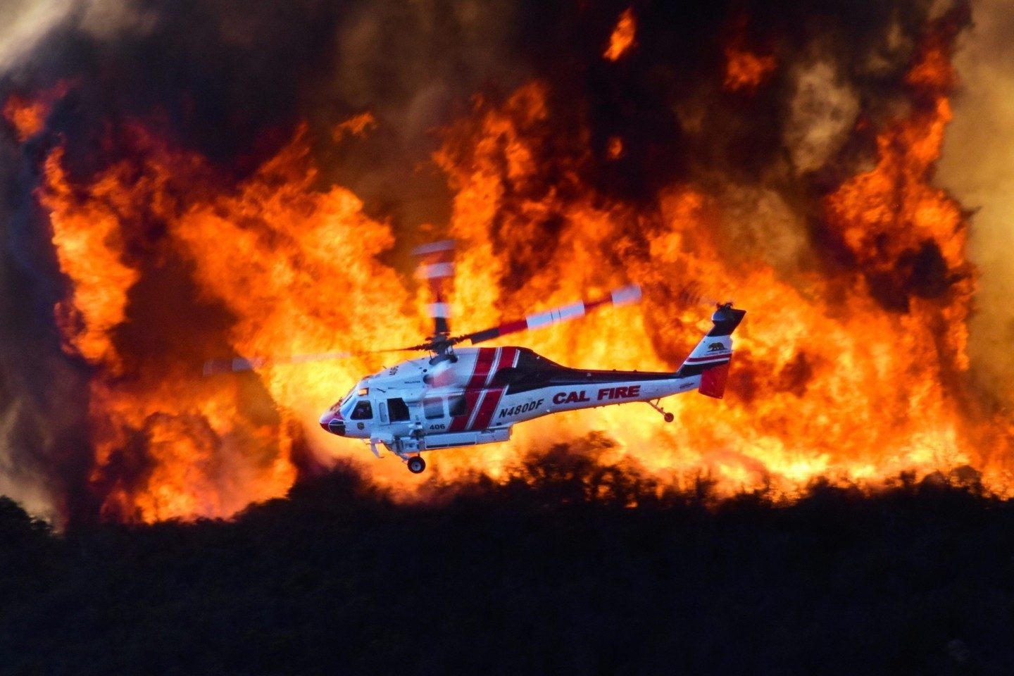 Cal Fire's Copter 406 comes out of the dipsite and crosses a wall of flame as they position themselves and look for the best place to drop
their load of water.