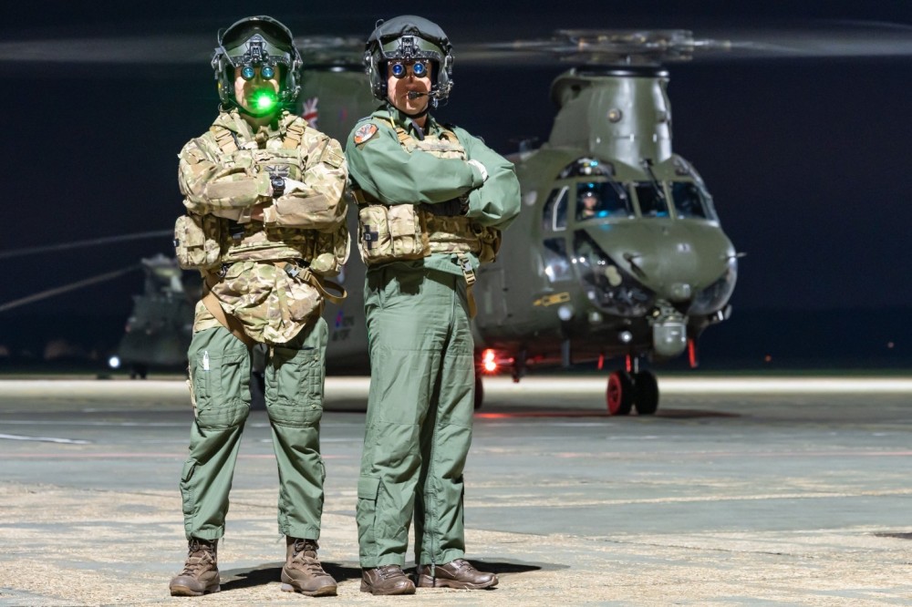 Pilots from the No. 27 Squadron of the British Royal Air Force posing in front of their Boeing Chinook HC6 military helicopter during a night shoot at RAF Odiham, UK.