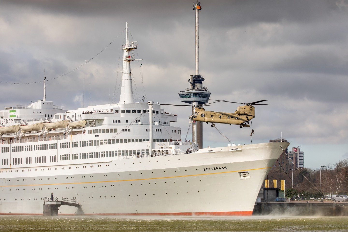 Dutch Air Force CH-47F is delivering troops through fastroping to the former Holland-America-line flagship SS Rotterdam during a training mission in Rotterdam. The ship, nowadays in use as a hotel, is featuring in this picture together with another famous Rotterdam landmark, the Euromast. There was only a brief spell of sunlight, pinching through the clouds at the right moment.