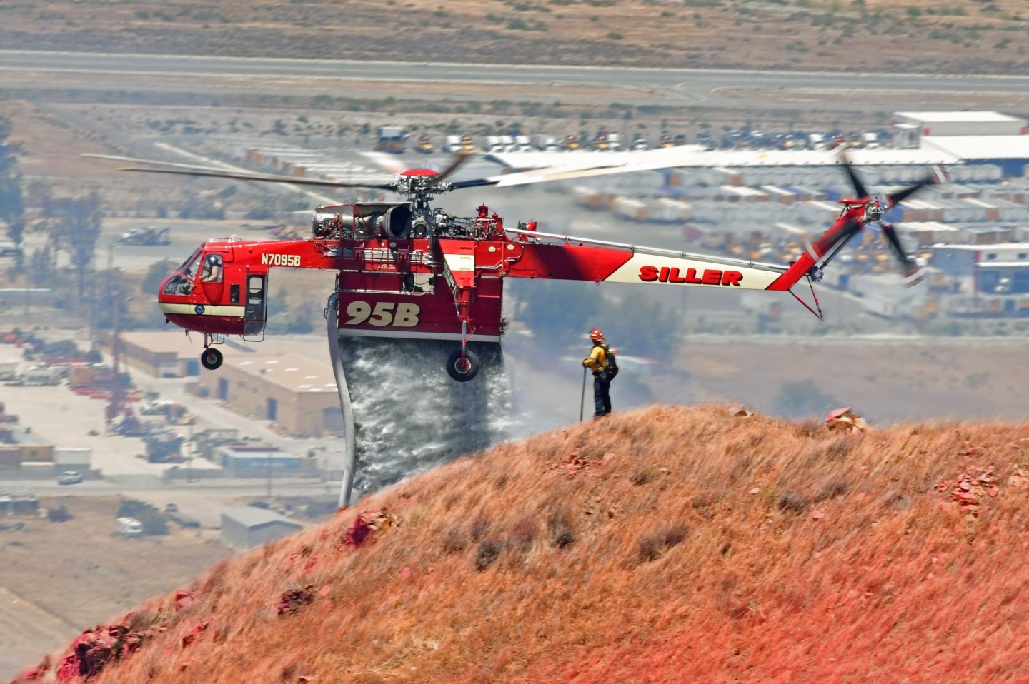 Siller Helicopters CH-54 Helitanker 95B makes a water drop on the Wolf Fire as a firefighter looks on.