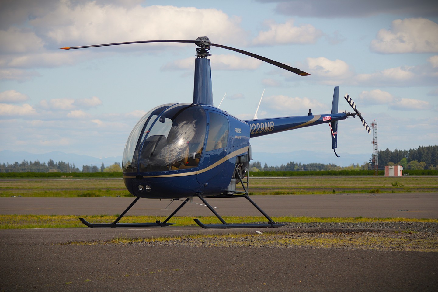 A flight school's Robinson R22 trainer sitting on the ramps during a warm summer afternoon. The photo captures the reflection of the sun and clouds in its crystal clear windshield.