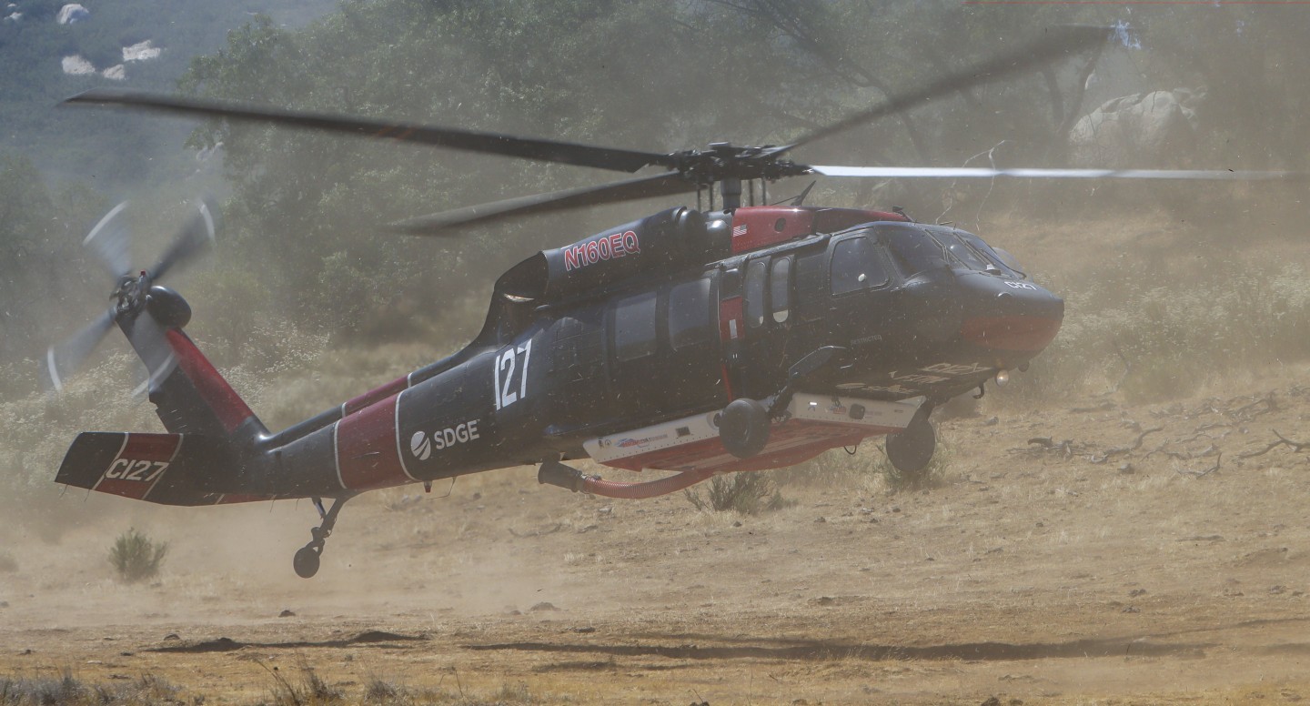 Copter 127 (operated by San Diego Gas & Electric), departing a dirt field after making water drops along a mountain ridge line, during the Springs Fire in July 2025.