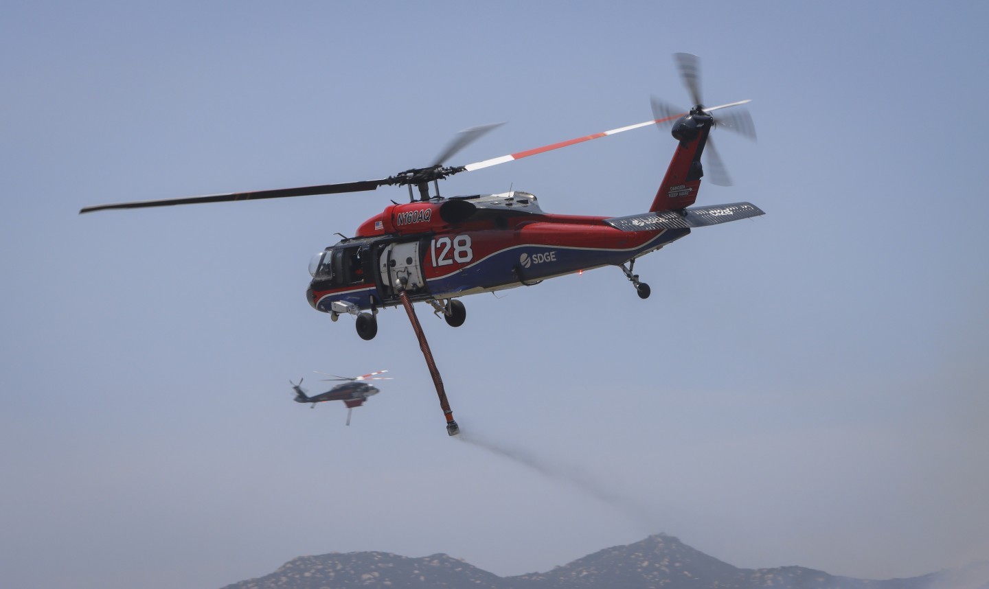 San Diego Gas & Electric Copter 128, and PJ Helicopters Copter 9PJ, cross paths as they return to the Monte Fire after dipping in the El Capitan reservoir of Lakeside, CA in June 2025.
