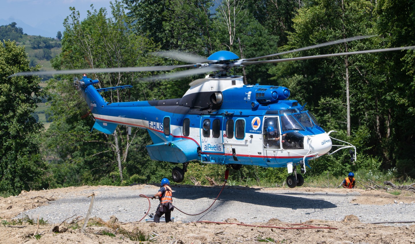 Airtelis Airbus H225 F-HLIS at the landing site during powerline works in the French Alps. The ground crew is manipulating the longline before the helicopter lands.