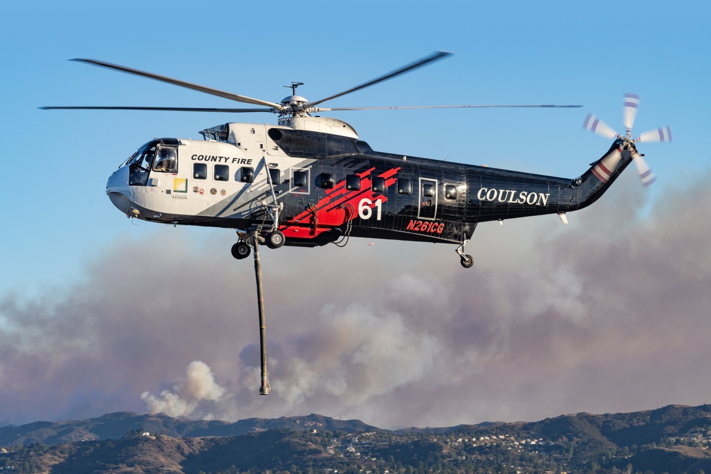 My son and I were photographing helicopters picking up water at the Encino Reservoir for the Palisades Fire, when we noticed a new fire at the Victory Trail area - Kenneth Fire. With traffic, it took us almost an hour to get there. We decided to hike a trail and climb a medium size hill where the fire fighters were working. The helicopters were going to a water tank bellow the hill so we were able to get eye level photographs. In this photograph of Coulson's Sikorsky S-61 coming back from dropping on the Kenneth Fire, you can see smoke from the massive Palisades Fire in the background. The city below is West Hills, California.