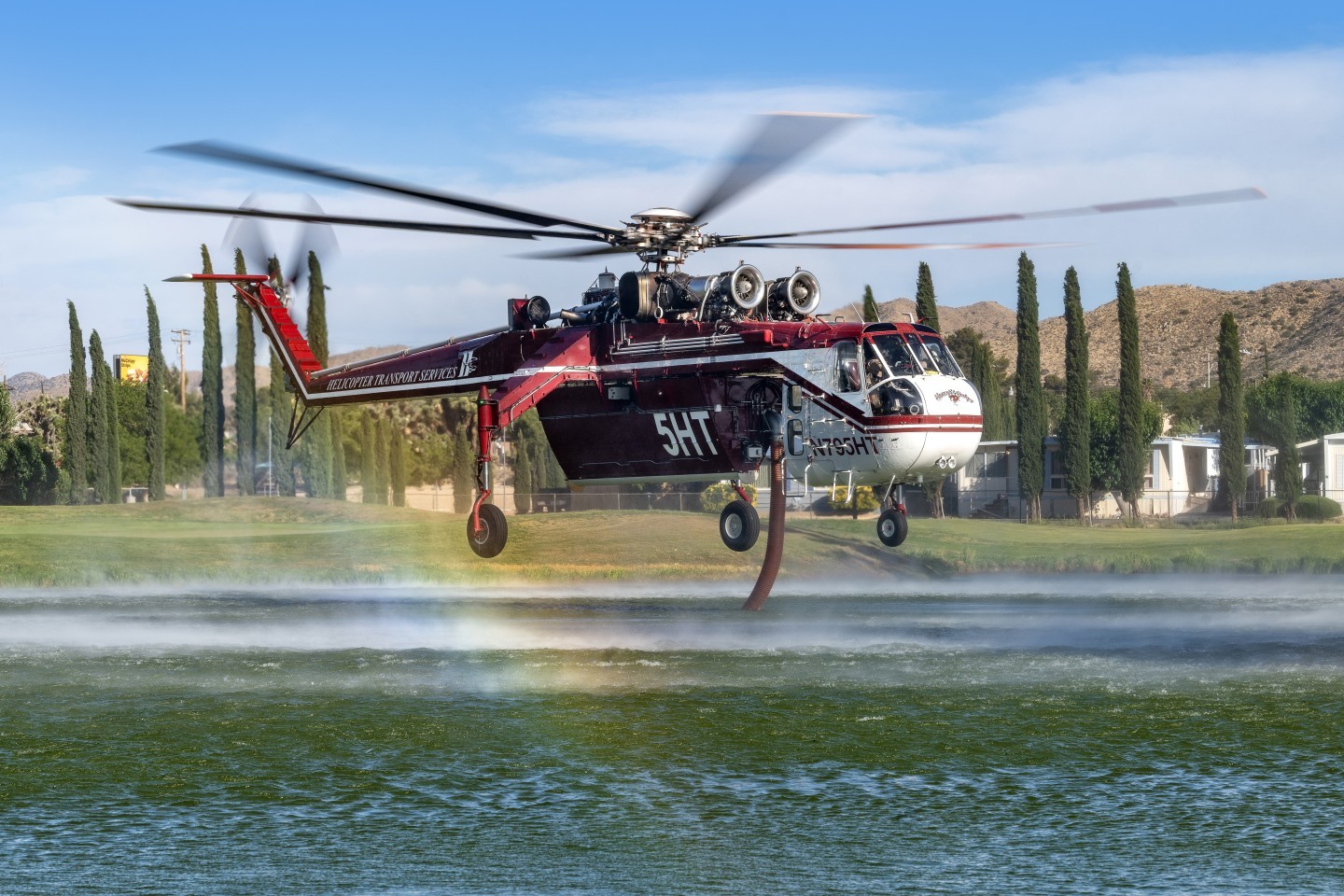 We got permission to go on Hawks Landing Golf Course to get helicopters picking up water for the Eureka Fire in Joshua Tree, California. In fact, they were so nice that they even let us use a golf cart to get to the small lake Helicopter Transport Services' Skycrane pilots skillfully maneuvered between trees and houses to pick up water. I photographed at a low angle so that the rainbow could be included.