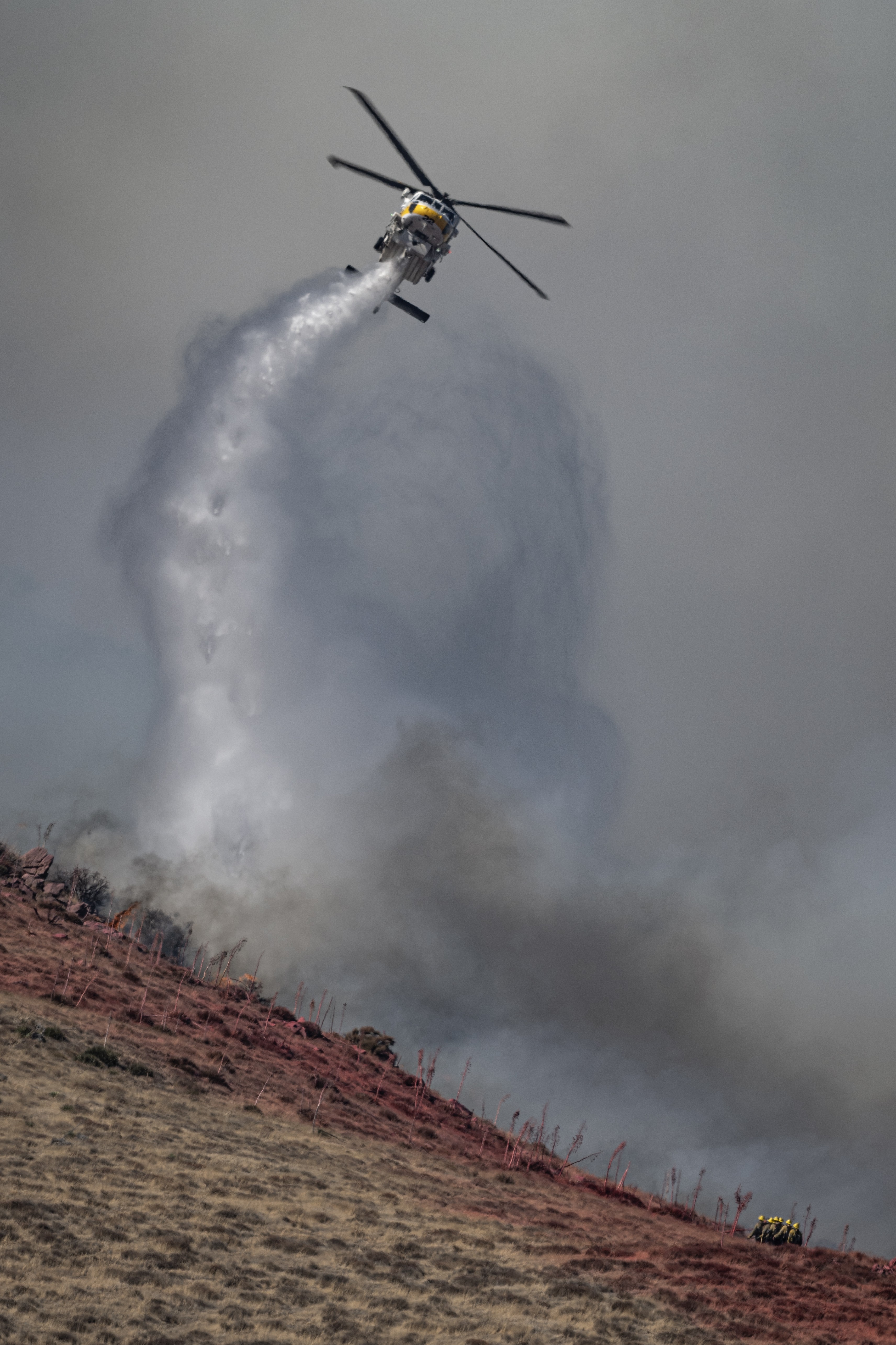 Los Angeles County Fire Department's Copter 22, a Sikorsky S70i, makes a water drop over fire crews during The Hawk Incident in Acton, California on August 14, 2025