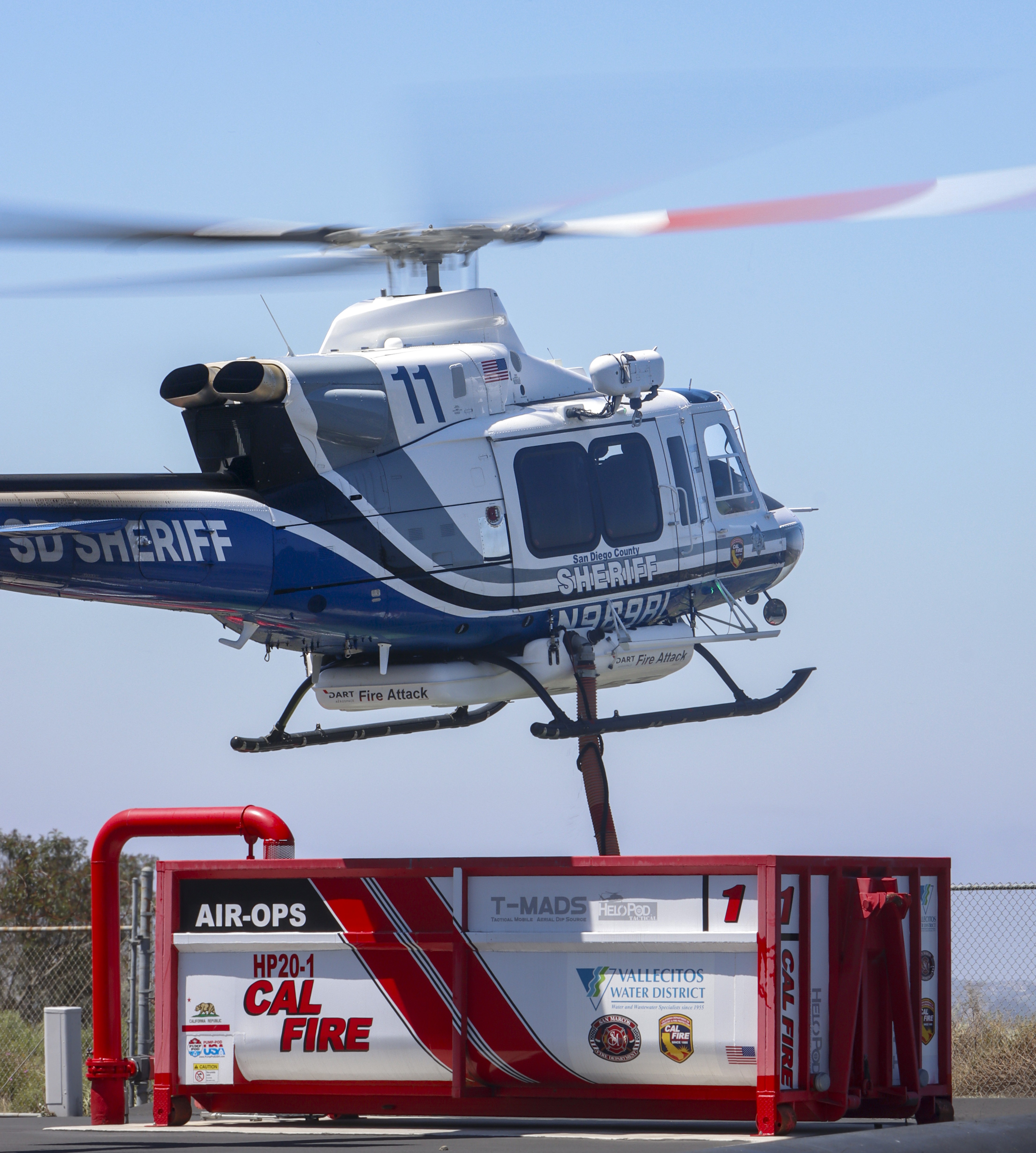A fairly brand new Bell 412EPX from the San Diego County Sheriff's Dept. hovers over a mobile water tank used for aerial firefighting, during an annual wildland drill in North County of San Diego, CA in May 2025.