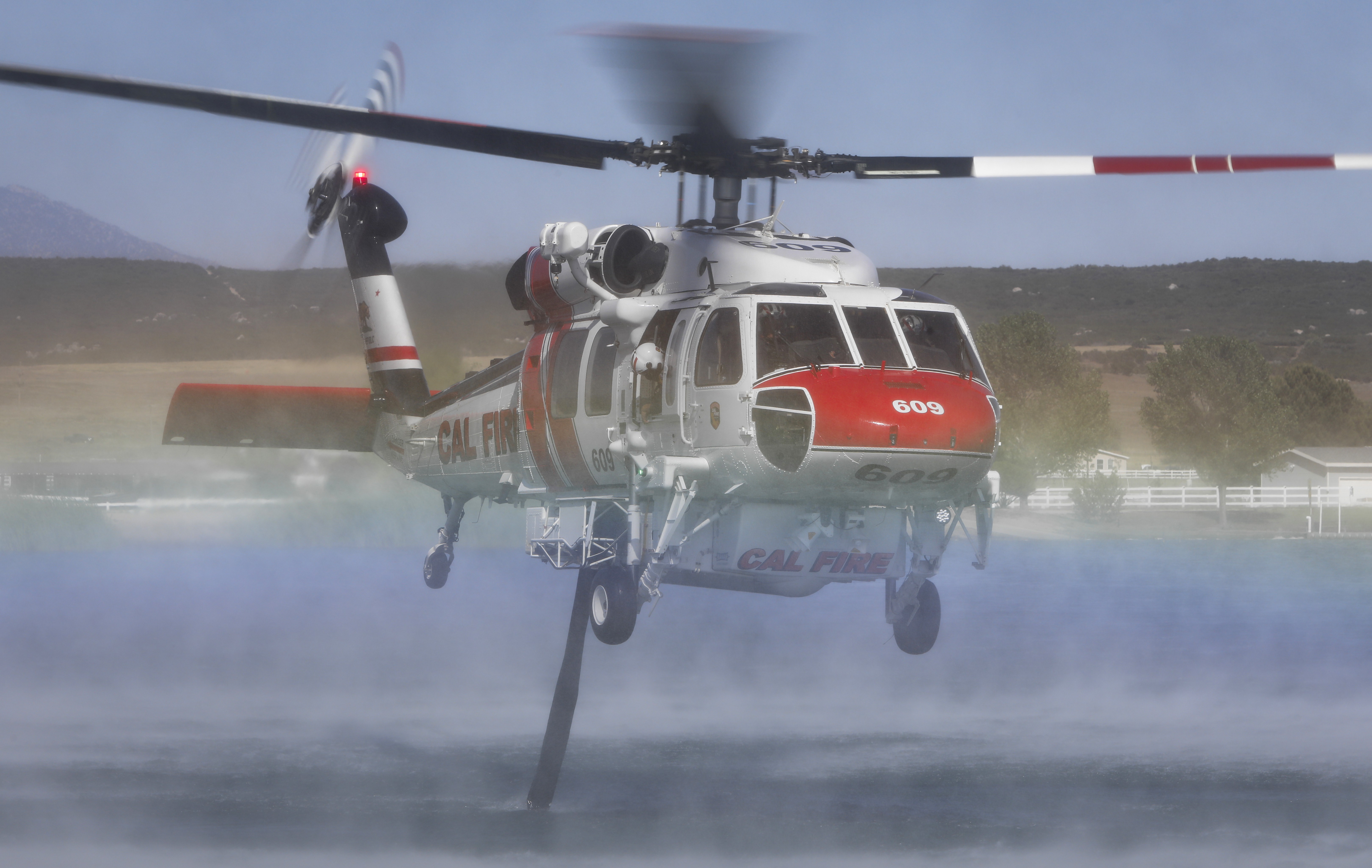 CAL FIRE Copter 609 taking a dip at Lake Riverside in Riverside County, CA during the Cahuilla Fire as a rainbow appears, reflecting off the water below.