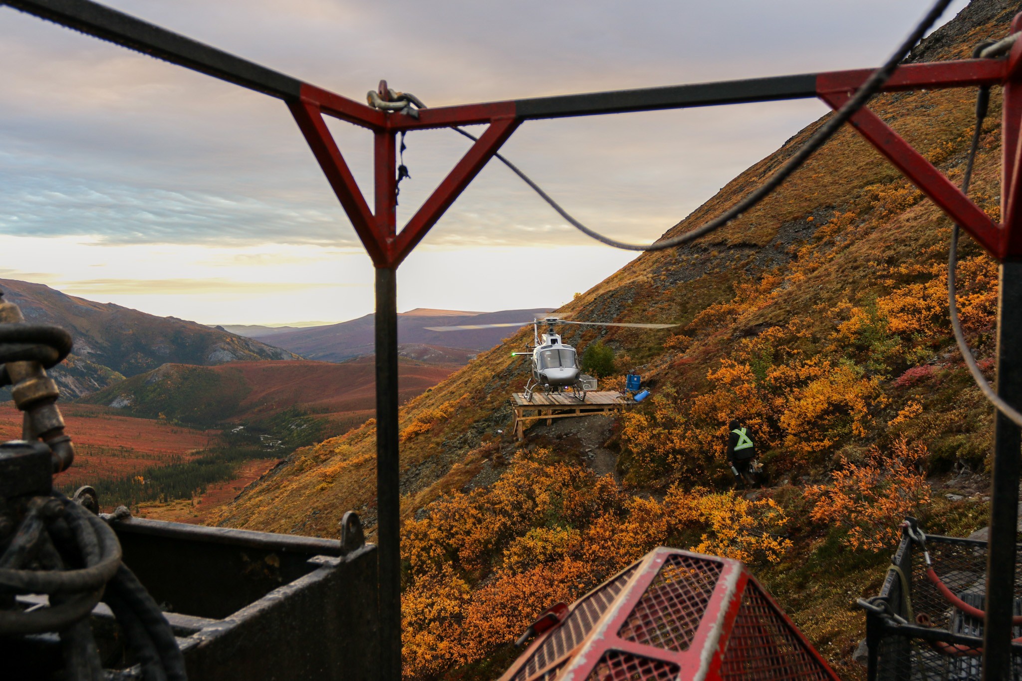 POV from the drill pad, driller walking to the helicopter during an early morning crew change from the drill site to camp. Located somewhere in the eastern Alaska Range mountains in early September. The fall foliage creating a beautiful back drop.