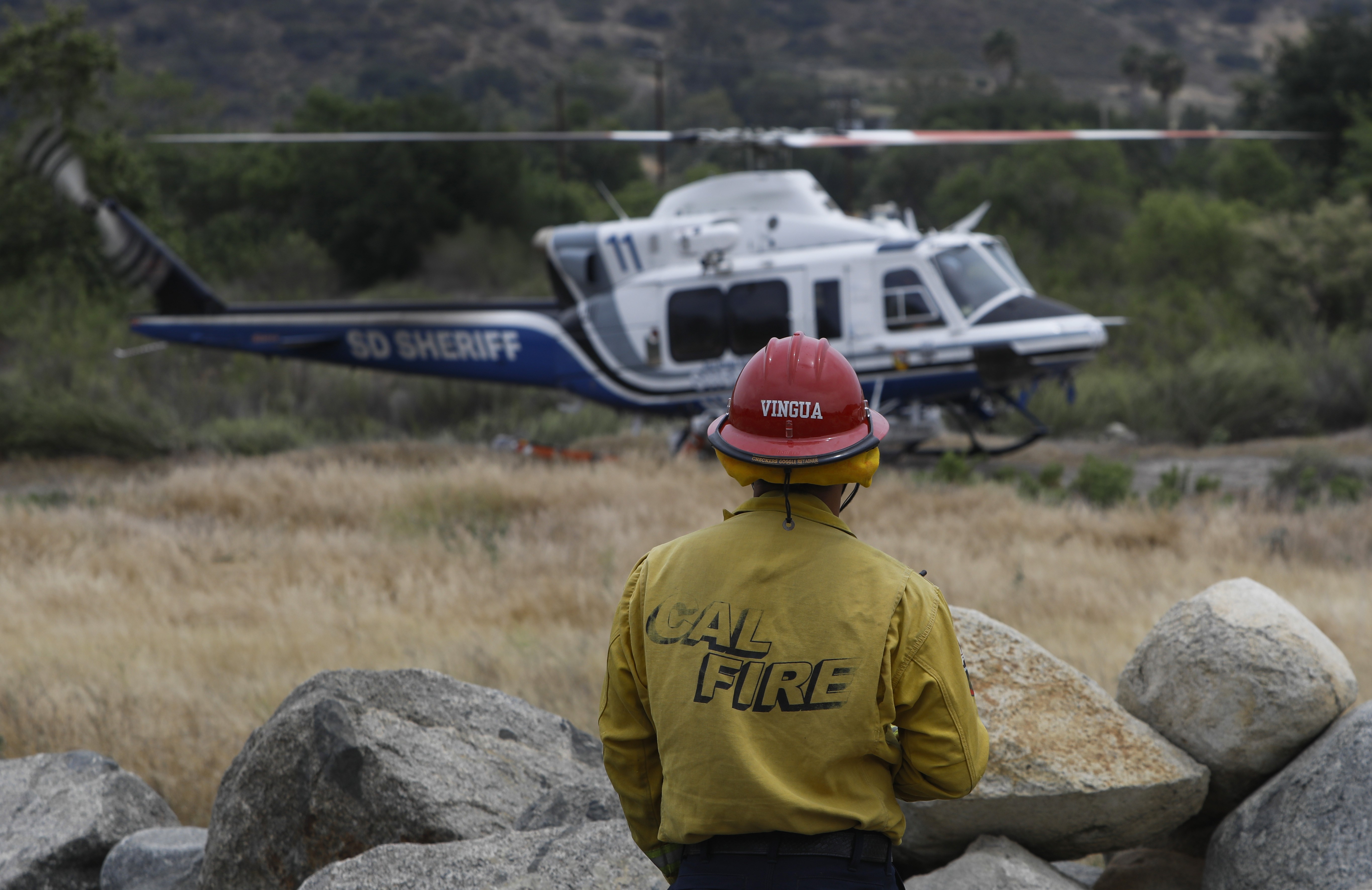 As Copter 11 from the San Diego County Sheriff's Dept. idles on the landing zone after returning for a fuel stop, a CAL FIRE helitack crewmember assigned to the copter waits for the pilot's permission to approach the active area.