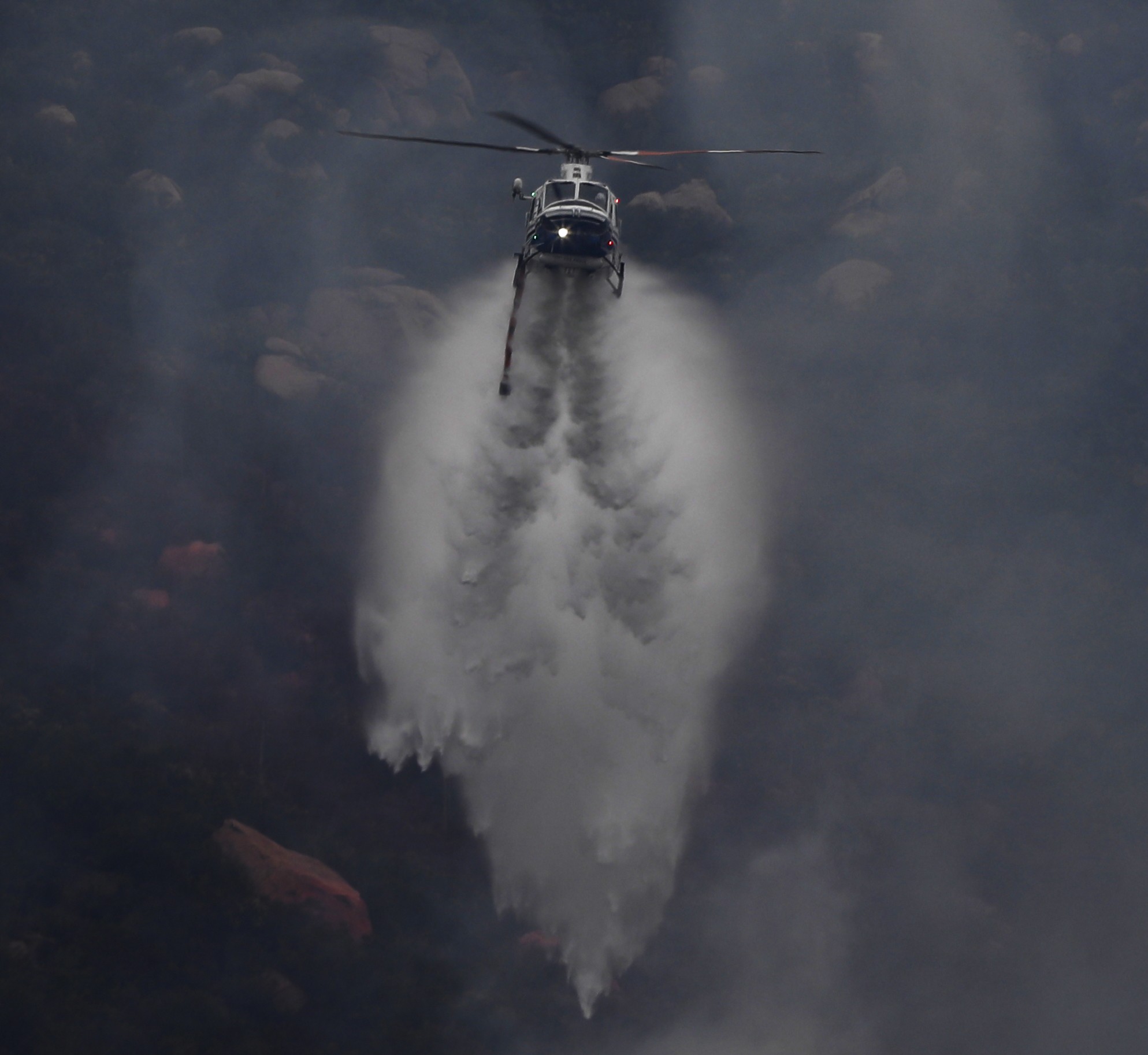 Copter 11 from the San Diego County Sheriff's Dept. creates vortices upon dropping water on hot spots part of a large vegetation fire during the Henderson Fire in Pala, CA.
