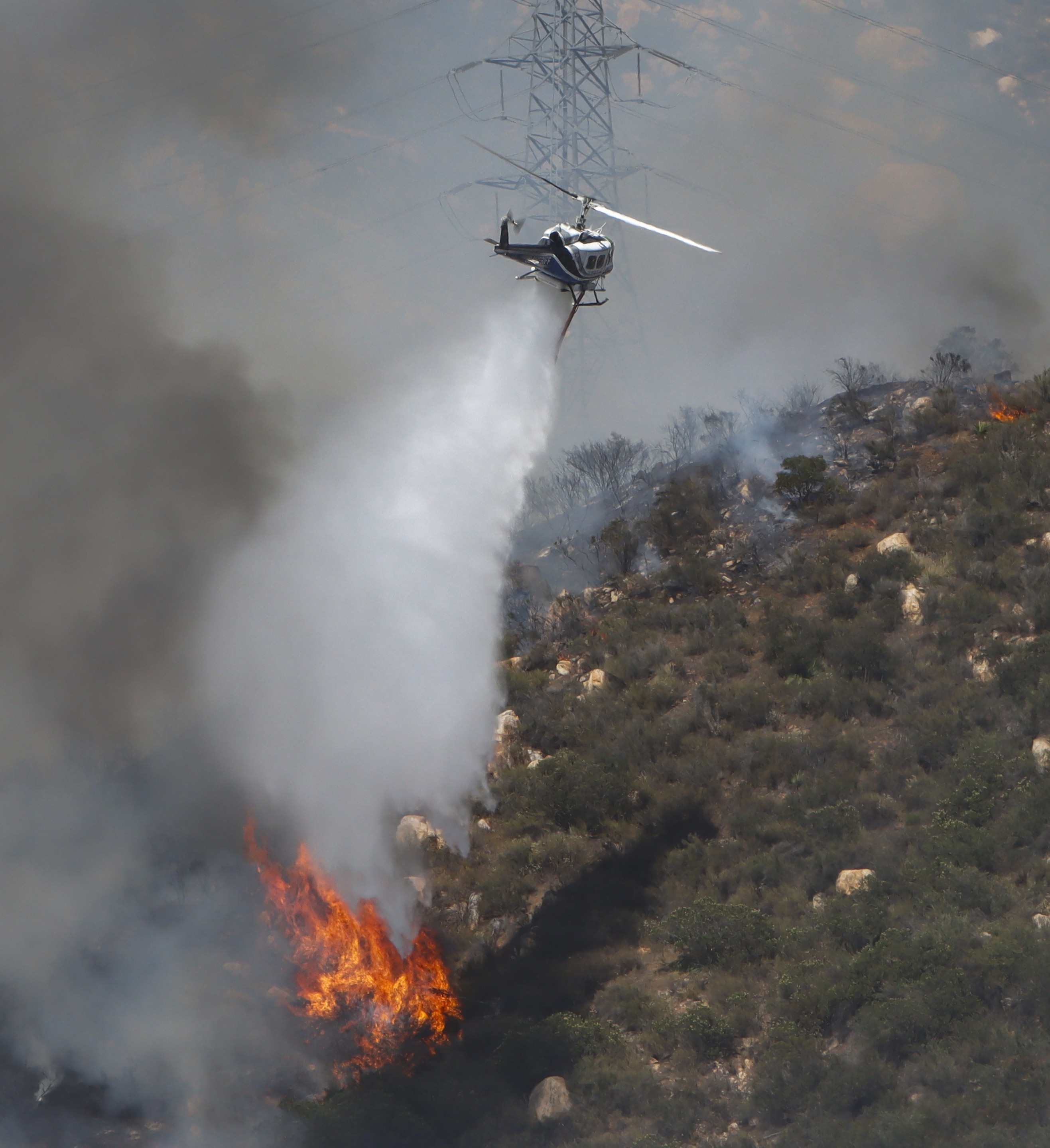 Copter 12 from the San Diego County Sheriff's Dept., making water drops on active flames in dense vegetation while supporting other firefighting agencies on containing a large vegetation fire in Lakeside, CA dubbed the Monte Fire.